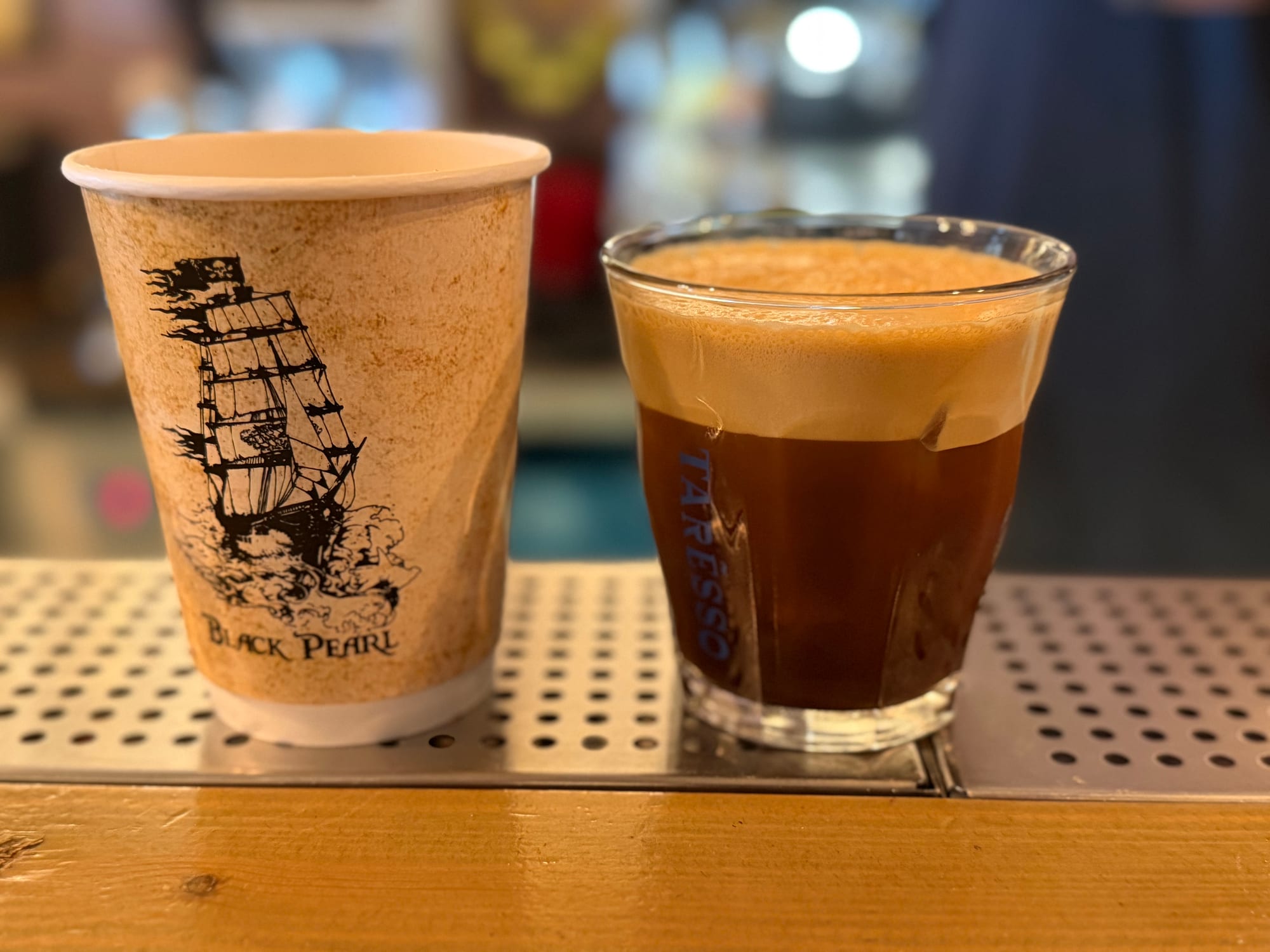 Black Pearl branded cup beside a glass of espresso